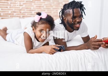 Vater und Tochter spielen Videospiel und liegen im Bett im Schlafzimmer Stockfoto
