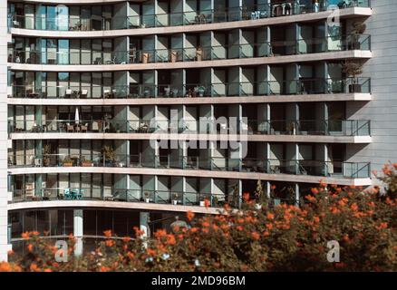 Die Glasfassade eines hohen, weißen Wohngebäudes mit Balkonen und gemusterten Fenstern und der strukturierte Hintergrund eines Wohnblocks Stockfoto
