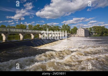 Fußgängerbrücke und Wasserdurchflusskontrolle über des Mille-Iles River und New Mill auf der Ile des Moulins Historic Site im Frühjahr, Old Terrebonne, Quebec. Stockfoto