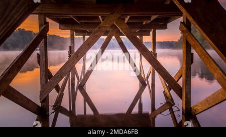 Ein hölzerner Dock erstreckt sich über einen ruhigen See an einem nebeligen Tag. Stockfoto