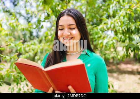 Lächelnde altmodische junge Frau, die ein Buch auf dem grünen Feld liest. Weltbuchtag. Stockfoto