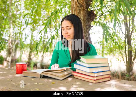 Teenager, die auf dem Feld unter einem Weidenbaum Bücher liest, mit einer Kaffeetasse. Weltbuchtag Stockfoto