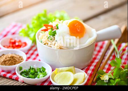 Nudelschüssel mit gekochtem Ei, Gemüse, Frühlingszwiebeln, Zitronensellerie, Salatsalat, Sellerie und Chili auf Holztisch, Instant-Nudeln, die kochen, schmackhaft essen Stockfoto