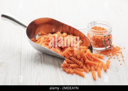 Rote Linsenfusilli-Pasta auf Holzhintergrund. Mit roher Pasta und roten Linsen füllen. Glutenfreie Nudeln. Stockfoto