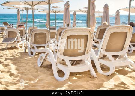 Reihen von Plastik-Liegestühlen am Sandstrand eines Hotels am Meer Stockfoto