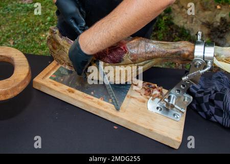 Ein professioneller Mann gibt dem Koch Handschuhe und schneidet den spanischen iberico-Schinken am Partytisch des Restaurants Stockfoto