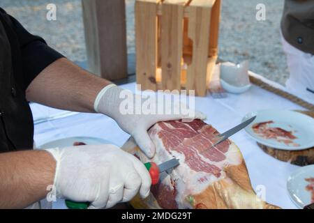 Roter Schinken, vom Küchenchef geschnitten, professionelles Schneiden von ganzen Knochen in serrano-Schinken Stockfoto