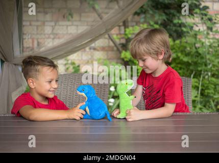 Zwei Jungen spielen mit weichen Dinosauriern an einem Tisch in Rollenspielen. Kommunikation mit Freunden, Freude, positiv. Lustige Aktivität für Freunde. Interessant ch Stockfoto