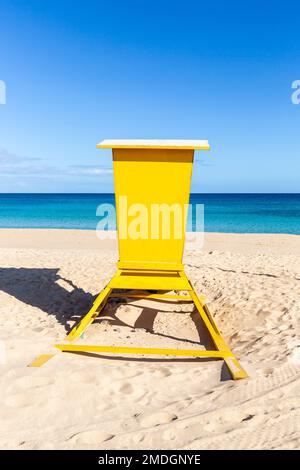 Hellgelbe Rettungsschwimmerkabine, die sich vor einem intensiven blauen Horizont erhebt. Stockfoto