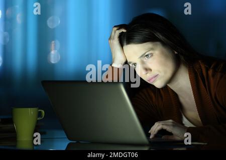 Eine besorgte Frau in der Nacht überprüft den Laptop zu Hause Stockfoto