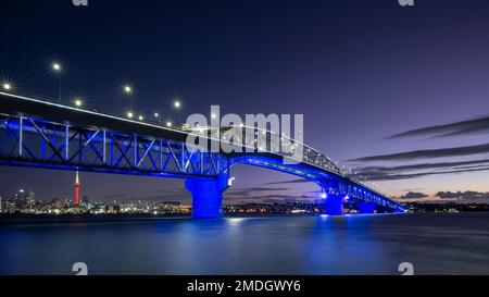 Die Auckland Harbour Bridge leuchtet blau. Skytower in Gold und Rot. Auckland, Neuseeland Stockfoto