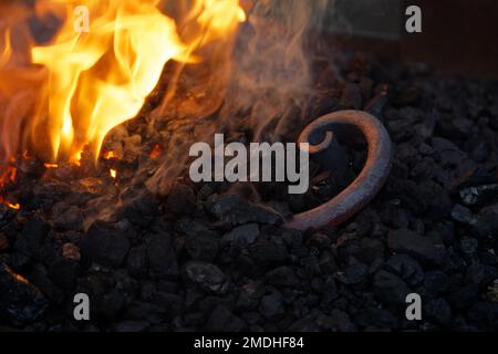 Spirale eines Eisenstabs, der in der Kohle des Schmiedefeuer liegt, der Schmied wird wieder erhitzt, Raum im dunklen Hintergrund kopieren, ausgewählter Fokus, n Stockfoto