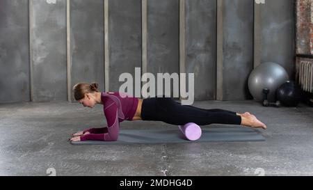 Eine junge Frau in Sportbekleidung führt eine myofasziale Hüftmassage mit einem Roller durch. Muskelerholung, Hersteller Stockfoto