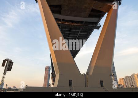 Ein Weibchen geht bei Sonnenuntergang an der großen, zweispaltigen, gebogenen Hängebrücke über den Fluss Chao Phraya vorbei. Thailand. Konzentrieren Sie sich auf die zwei-Säulen-Kurve. Stockfoto