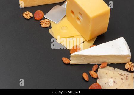 Verschiedene Käsesorten auf einem Holzbrett mit Trauben, getrockneten Aprikosen und Nüssen Stockfoto
