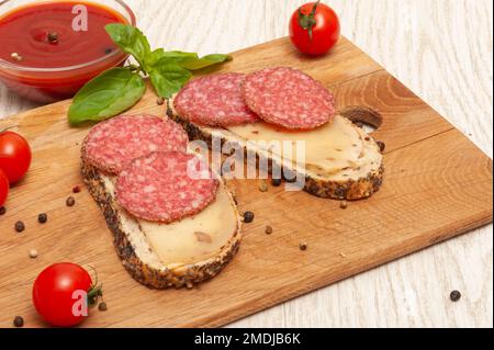 Sandwiches mit Räucherwurst und Käse auf einem Holzbrett, dekoriert mit Kirschtomaten und Basilikum Stockfoto