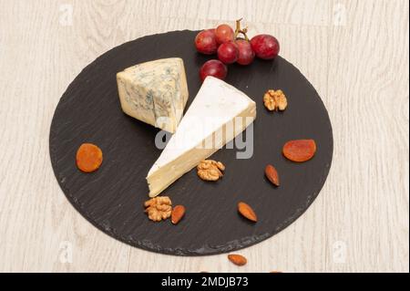 roquefort-Käse und Brie auf schwarzem Graphitbrett mit getrockneten Aprikosen und Nüssen Stockfoto