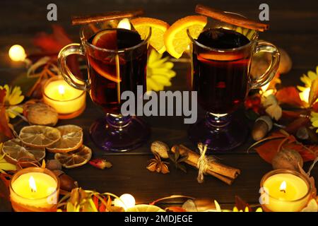 Becher Glühwein mit Dekoration und Kerzen auf dunklem Holzhintergrund Stockfoto