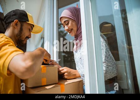 Ein hübsches Mädchen, das einen Hijab trägt, bekommt Waren von Liefermännern Stockfoto