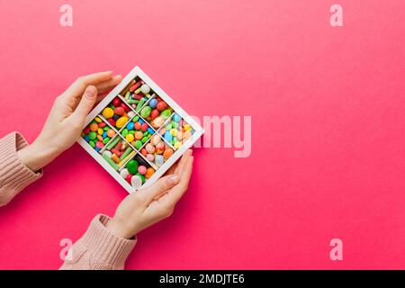 Weibliche Hände mit köstlichen Süßigkeiten in der Schachtel auf farbigem Hintergrund. Stockfoto