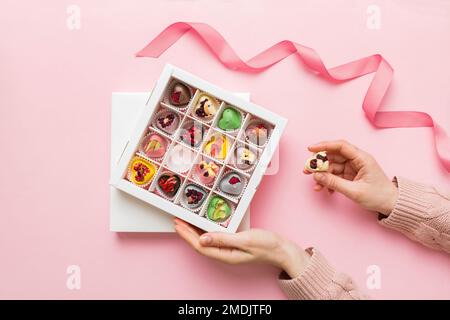 Weibliche Hände mit köstlichen Süßigkeiten in der Schachtel auf farbigem Hintergrund. Stockfoto