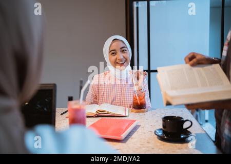 Wunderschönes Hijab-Mädchen, das sich unterhält, während es mit Freunden trinkt Stockfoto
