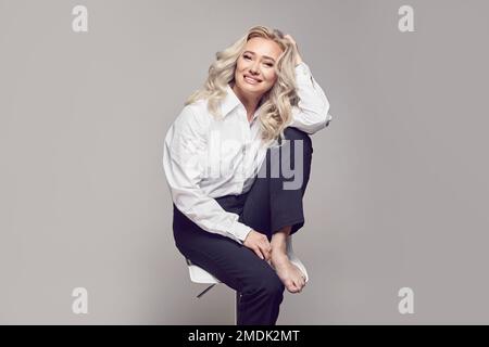 Frohe Reife. Charmante, reife Frau, die aufrichtig lächelt auf einem grauen, isolierten Hintergrund mit einem freien Werbespot. Stockfoto