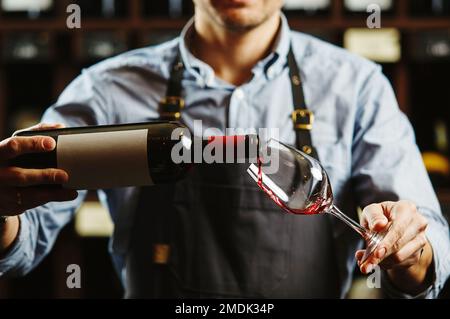 Sommeliermännchen gießt Rotwein in langstielige Weingläser. Stockfoto