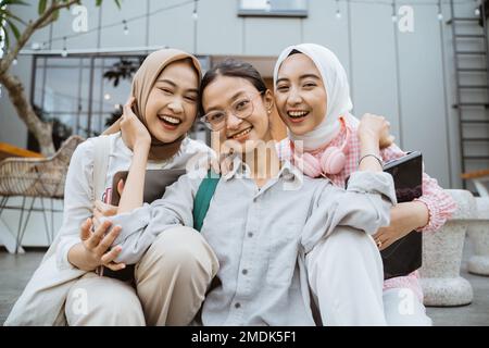 Drei asiatische Schülerinnen lächeln, während sie zusammen im Café sitzen Stockfoto