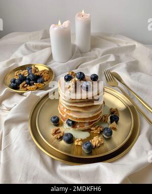 Ein vertikaler Schuss Pfannkuchen auf einem weißen Teller mit Kondensmilch und Heidelbeeren und Walnüssen darauf Stockfoto