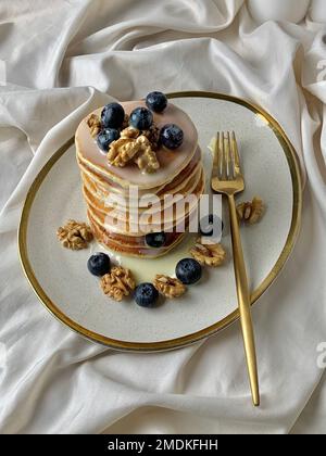 Ein vertikaler Schuss Pfannkuchen auf einem weißen Teller mit Kondensmilch und Heidelbeeren und Walnüssen darauf Stockfoto