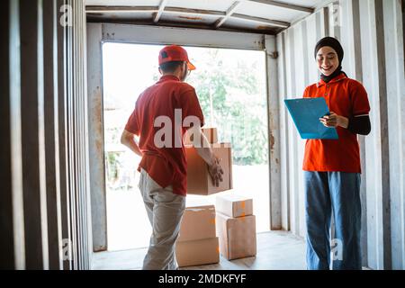 Weibliche Arbeiter zum Überprüfen und männliche Arbeiter heben Kisten Stockfoto