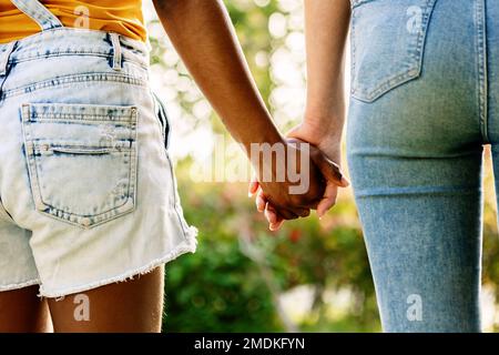 Multirassisches junges weibliches Paar, das draußen Händchen hält Stockfoto