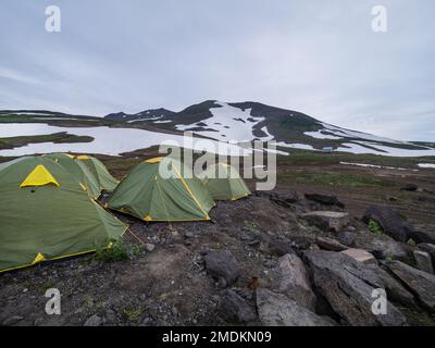 Grüne touristische Zelte am Berghang auf der Halbinsel Kamtschatka. Aktivtourismus im Sommer in Russland. Stockfoto