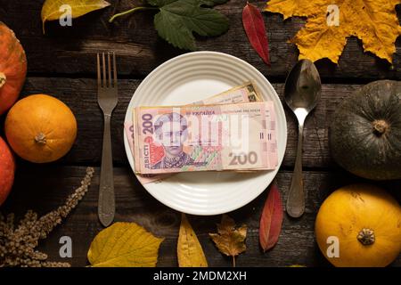Die Banknoten von hundert zweihundert Hrywna liegen auf einem Teller auf einem Holztisch im Herbstdekor, mit Blättern und Kürbis, ukrainisches Geld auf dem Tisch, ich Stockfoto