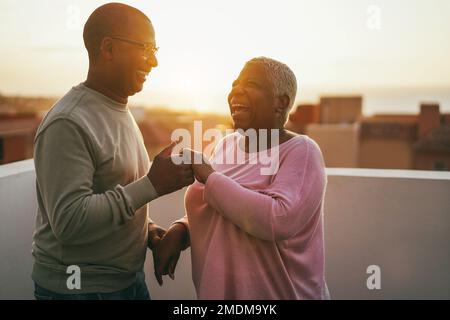 afrikanisches Seniorenpaar tanzt im Freien mit Sonnenuntergang im Hintergrund - Focus on Stockfoto