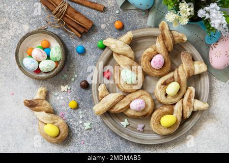 Osterbackidee. Osterhasen-förmige Brötchen pusten Gebäck mit Zimt auf einem Steintisch. Blick von oben. Stockfoto