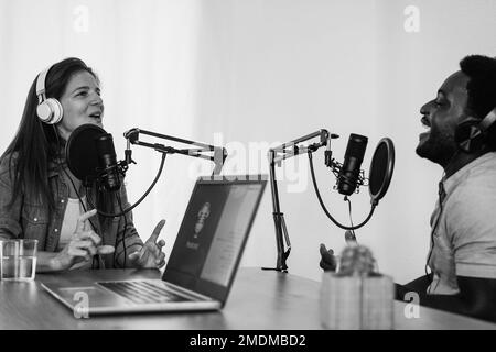Multiethnische Moderatoren streamen Podcasts im digitalen Studio - Weiche Fokussierung auf weibliches Gesicht - Schwarzweiß-Bearbeitung Stockfoto