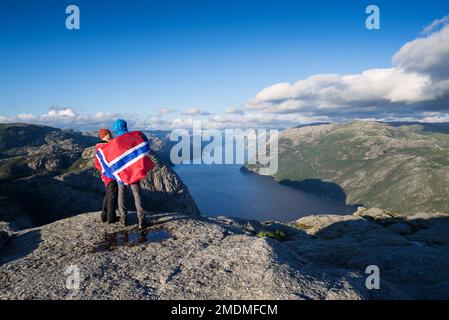 Weg Preikestolen, Norwegen. Paar mit der Flagge von Norwegen. Panorama der Lysefjord Stockfoto