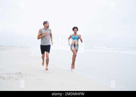 Mehr frische Luft bedeutet weniger Ermüdung. Ein junges Paar, das zusammen am Strand entlang läuft. Stockfoto