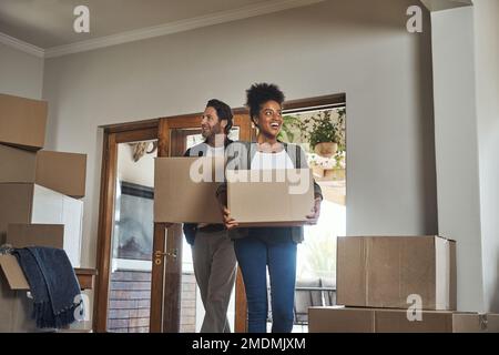 Wir haben das perfekte Zuhause gefunden. Ein junges Paar, das lächelt, während es Kisten in sein neues Zuhause trägt. Stockfoto