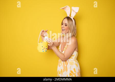 Junge Frau Studio isoliert auf Gelb mit Hasenohren, die Eier neugierig halten Stockfoto