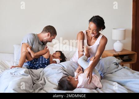 Jeder Morgen mit ihnen ist etwas Besonderes. Eine wunderschöne, junge vierköpfige Familie, die sich zu Hause im Bett anfreundet und Zeit miteinander verbringt. Stockfoto