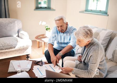 Sie planten einen komfortablen Ruhestand und sie haben ihn bekommen. Ein älteres Paar, das zu Hause Papierkram durchsucht. Stockfoto