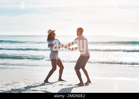 Sei dumm und hab Spaß mit dem, den du liebst. Ein junges Paar, das am Strand tanzt. Stockfoto