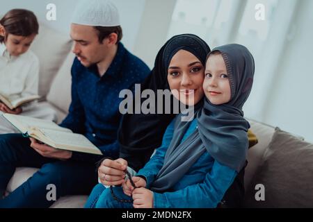 Glückliche muslimische Familie genießt den heiligen Monat des Ramadan, während sie zusammen in einem modernen Haus betet und den Koran liest Stockfoto