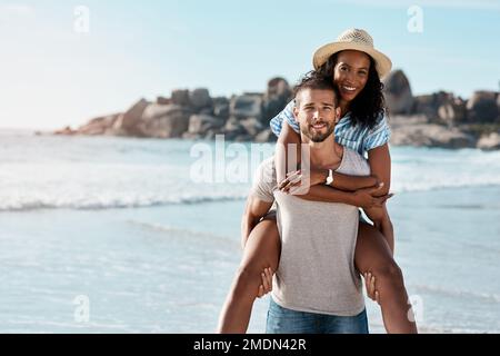 Es ist bei weitem unser Lieblingsurlaub. Porträt eines jungen Mannes, der seine Freundin am Strand mit dem Huckepack betritt. Stockfoto