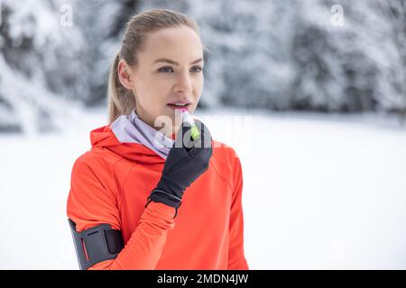 Eine junge Läuferin trägt aufgrund des frostigen Wetters einen schützenden Balsam auf ihre Lippen auf und verhindert so das Aufreißen und Trocknen der Lippen. Stockfoto