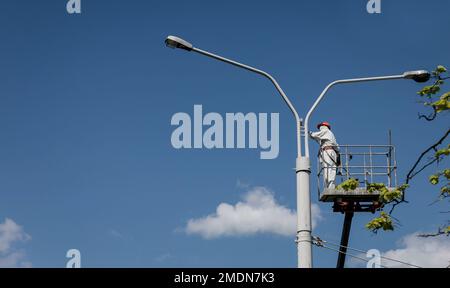 Ein Mann steht auf einem Turm und malt einen Laternenpfahl. Männer in der Wiege malen Lampenpfähle Stockfoto