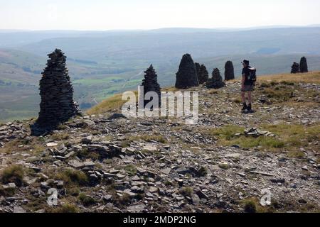 Ein Mann, der an den Stone Cairns auf dem Gipfel der Yoadcomb Scar on Wild Boar Fell im Eden Valley vorbeigeht, Yorkshire Dales National Park, England, Großbritannien Stockfoto